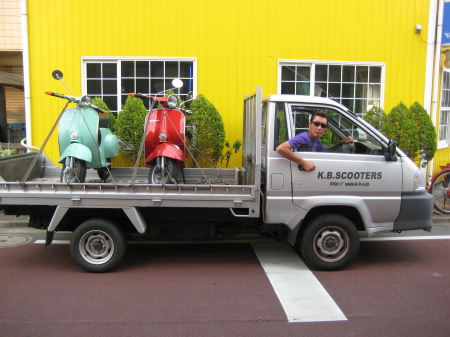 K.B.SCOOTERSのトラックに積載された2台のベスパと店前に停車する様子
