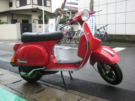 雨に濡れた路肩に停車している赤いベスパPX200FL