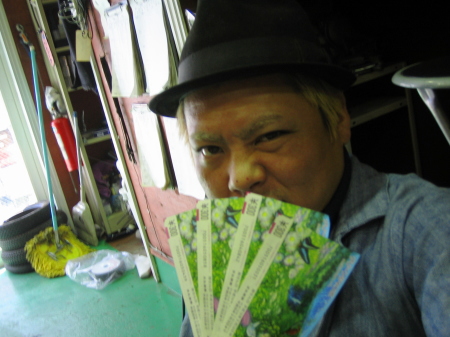 宝くじ当選券を手にした店主の笑顔。冗談交じりの喜びが伝わる。