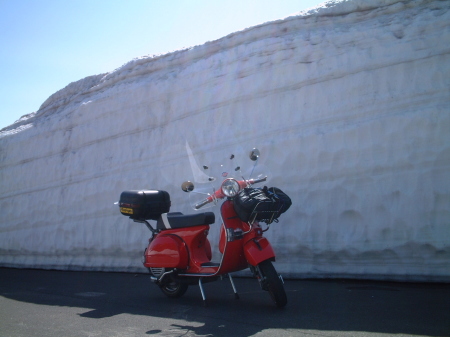 雪の壁の前に停車する赤いベスパ。ツーリング途中の記念撮影。