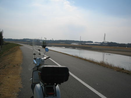 河原沿いの道に停車した白いベスパ。穏やかな冬晴れの景色