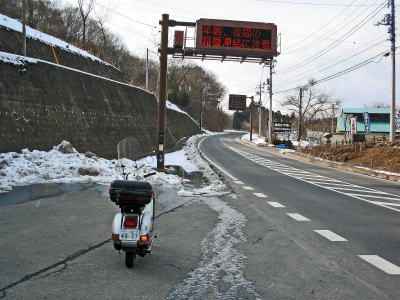 雪が残る道路に停車したベスパと電光掲示板の「積雪注意」の表示