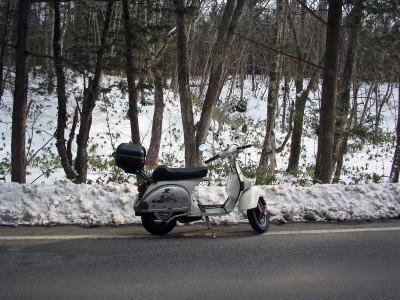 雪の残る林道の路肩に停められた白いベスパP200E