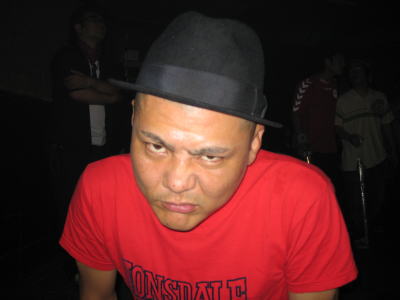 LONSDALEの赤シャツを着た男性が帽子をかぶって睨むようにカメラを見ている