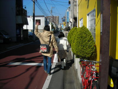K.B.SCOOTERSを後にし、手を振る未来のオーナー夫妻の後ろ姿。晴れた道沿いにて