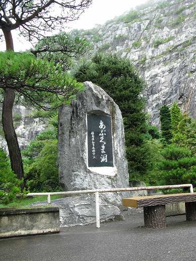 青の洞門の入り口に立つ記念碑。岩壁と松の木に囲まれた静かな風景。