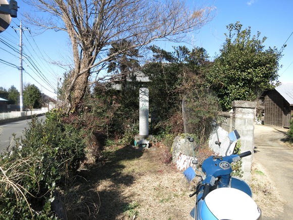 道路沿いの木々に囲まれた鳥居と、その手前に停められた青いベスパ
