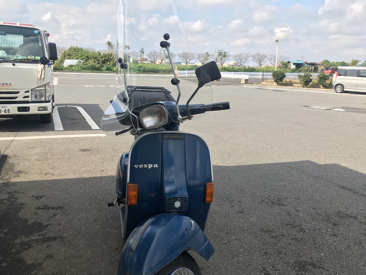 駐車場に停めた青いベスパと、奥に見える成田ゆめ牧場の建物