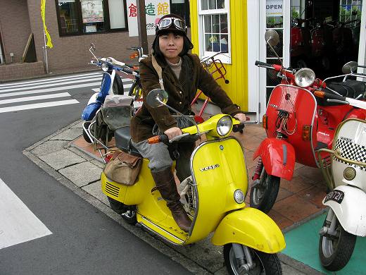 黄色いベスパに乗った女性のお客様と店舗前の風景