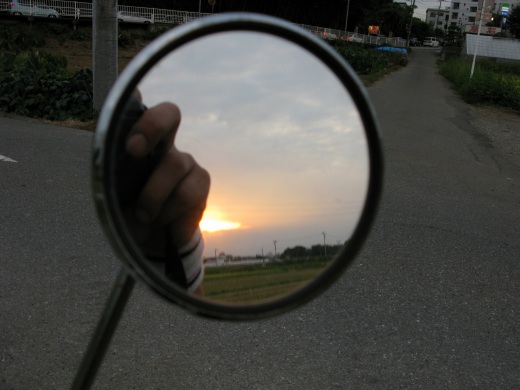 バックミラー越しに見える夕日と田園風景