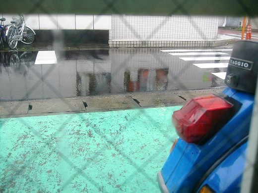 店舗の窓越しに見える雨の道路と青いベスパのリアビュー