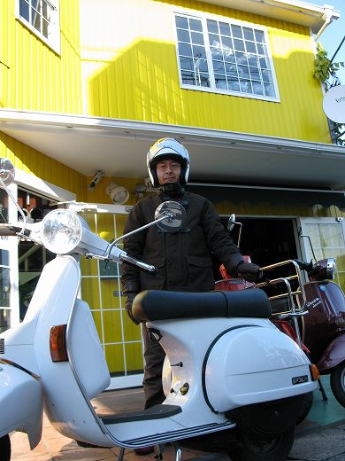 店舗前で撮影された赤いベスパPXのスピードメーター越しの街並み。