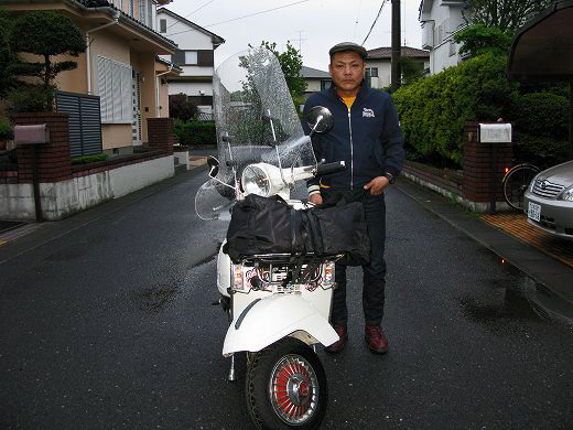 出発直前、雨の中で白いベスパと並んで立つライダーの写真