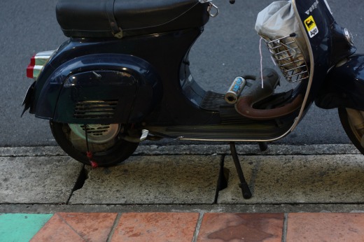 歩道の段差にスタンドをかけて停車しているネイビーのVespa 50s