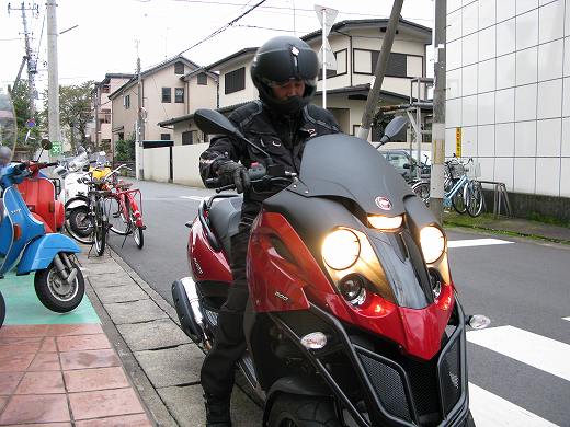 赤と黒の三輪スクーターFUCCOの横でヘルメットを持ち立つ男性