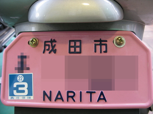 成田市の原付ナンバープレート。ピンク色に「NARITA」のローマ字が入っている。