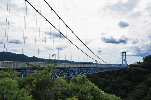 竜神大吊橋を斜めから見上げた迫力ある光景。山々と曇り空を背景に架かる青い吊橋