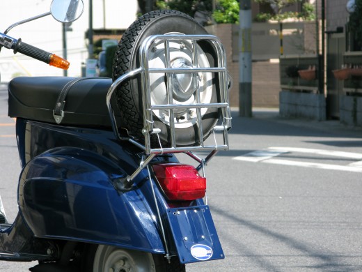 青いベスパに取り付けられたメッキ仕上げのリアキャリアとスペアタイヤ