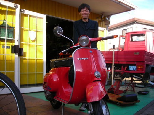 納車された赤いベスパ50Sとそのオーナーが店先で撮影された記念写真