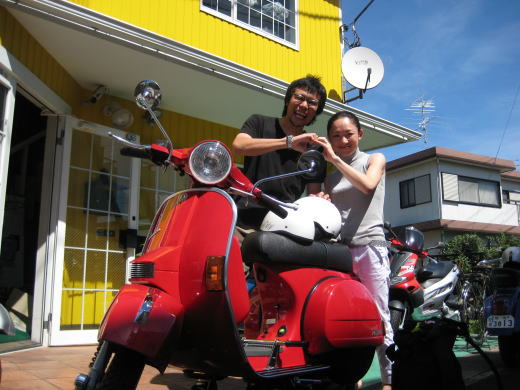 赤いベスパの前でハートマークポーズをとる夫婦