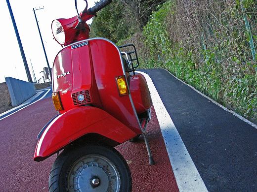 カーブ道に停車した赤いベスパのリアビュー