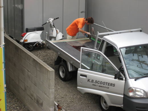 トラック荷台の板にペンキを塗っているK.B.SCOOTERSの作業風景