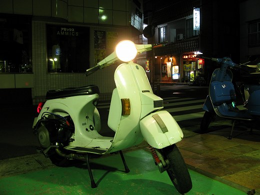 夜の街角に停められた白いベスパ