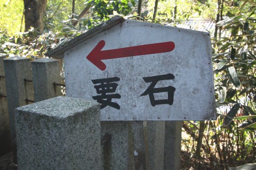 「要石→」と書かれた案内板と石柱が並ぶ森の中の様子