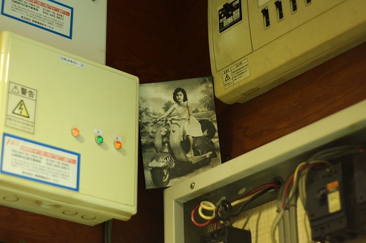 電気設備の壁に飾られたベスパに乗る女性のモノクロ写真