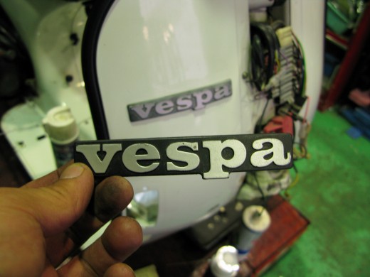 ヤレたvespaエンブレムを持ち、新しいものと交換作業中