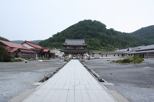 山を背にして佇む寺院の正門。長い石畳が一直線に伸び、荘厳な雰囲気が漂う