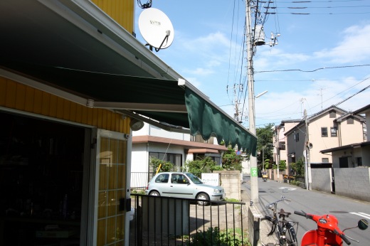 店先に設置された緑のテントと赤いベスパ