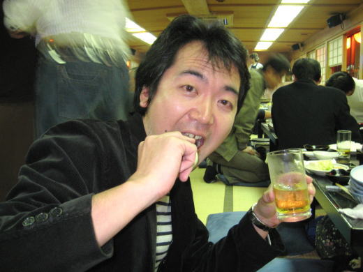 縞シャツ姿の男性がつまみを手にお酒を楽しむ場面
