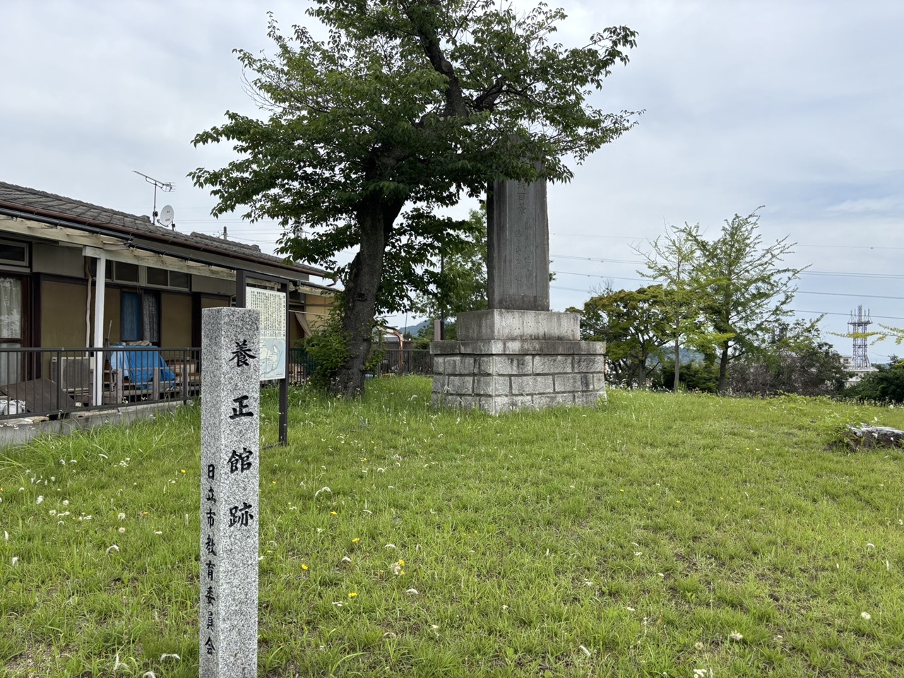 養正館跡の石碑とその周辺の草地。背後には古い住宅が見える。