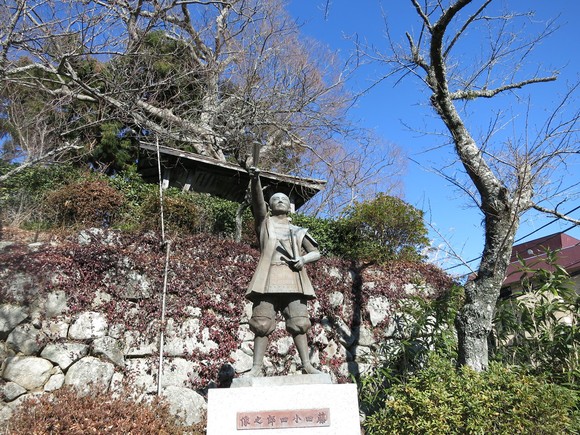 槍を掲げる少年像と背後の木々が印象的な石垣の風景