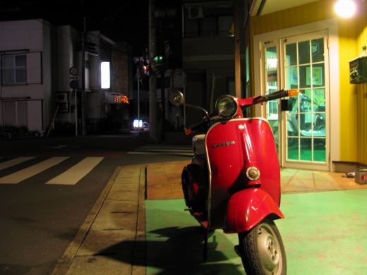 夜の柏の街角に停められた赤いベスパ