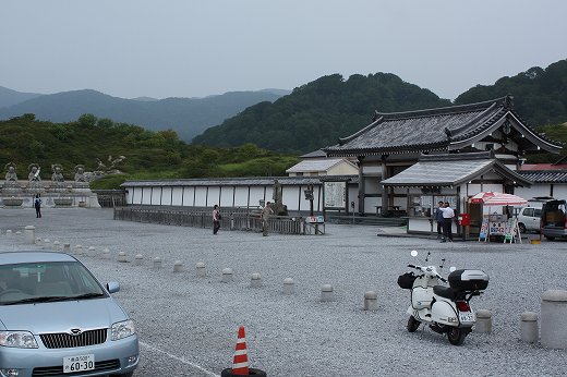 寺院の前に停まる白いベスパと車。広い砂利の駐車場に穏やかな日常感が漂う風景