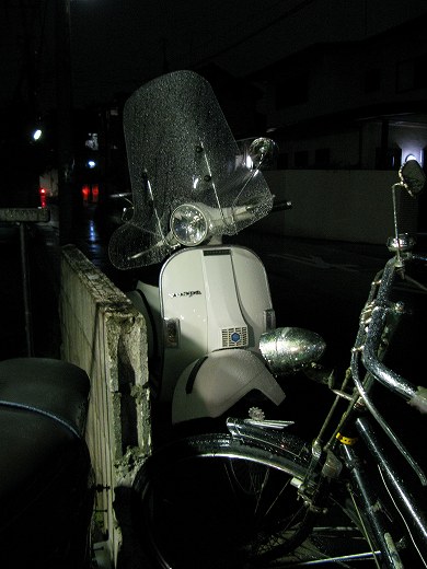雨に濡れながら停車しているベスパ50sとその周囲の風景。