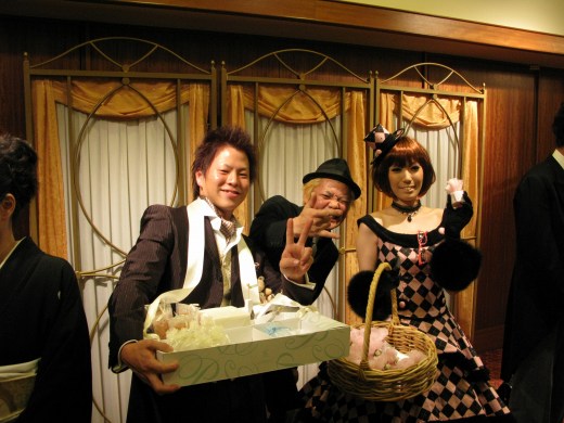 結婚式場で新郎新婦と記念撮影する店主。笑顔とピース。