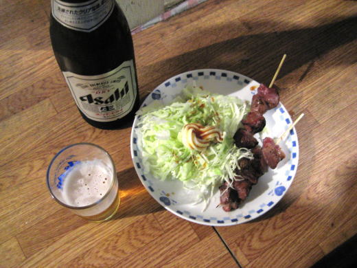 立ち飲み屋のカウンターに並んだ瓶ビールと焼き鳥とキャベツの皿