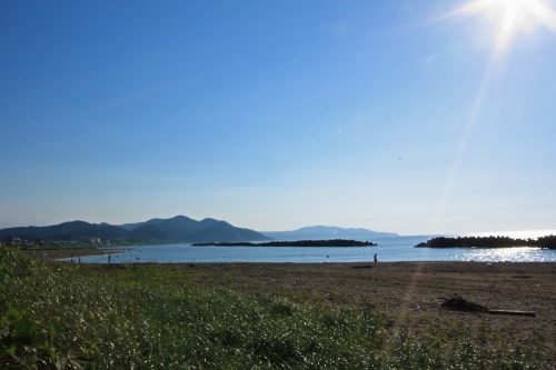 日本海に沈む夕日が差し込む海岸線。静かな波と光のコントラストが美しい風景。