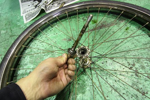 古い自転車の前輪ハブから抜き取られた、固着したグリスの付いたシャフト。
