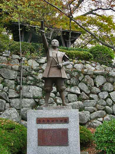 拳を掲げた藤田小四郎像と石垣の背景
