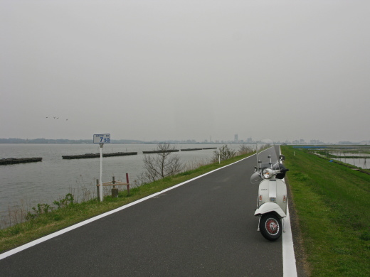 霞ヶ浦湖畔の堤防道路を走る白いベスパの後ろ姿