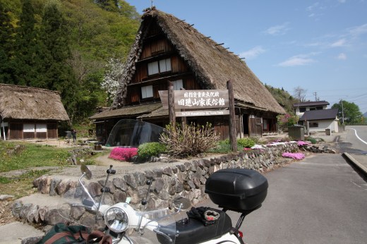 合掌造りの古民家とベスパ、春の花に囲まれた山里の風景