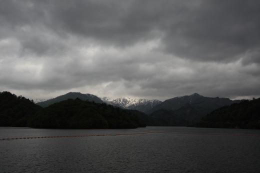 奥利根湖とその奥にそびえる雪をかぶった山々、曇り空の風景