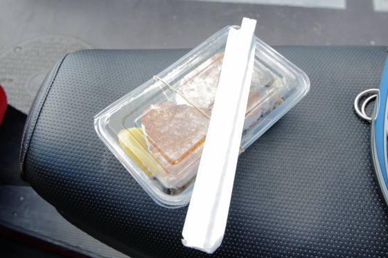 ベスパのシートの上に置かれた、焼きおにぎり弁当