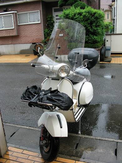 雨上がりの路上に停まる白いベスパ。大型ウインドシールドが装備されている。