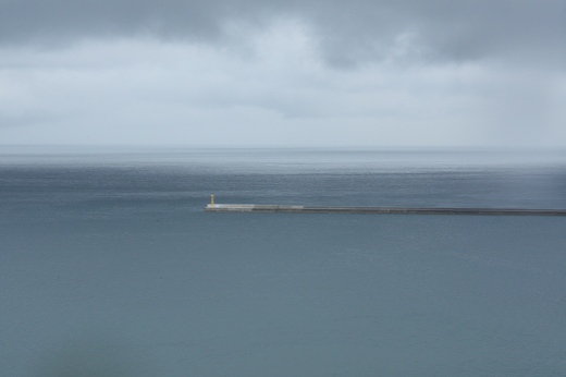 雲が垂れ込める海に伸びる防波堤。静けさと広がりが感じられる風景