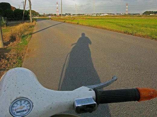 田んぼ道に伸びるベスパとライダーの影